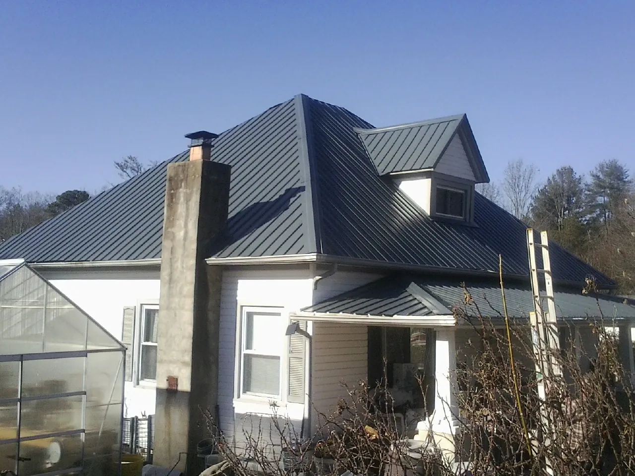 Dark blue standing seam metal roof on a white farmhouse with dormer — Slate & Tile Roof Repair by Roofing Brothers in Piedmont