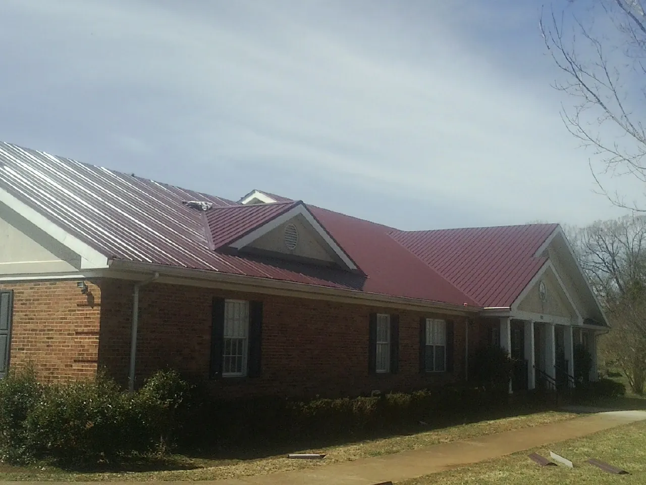 Red metal roof with gabled entries on a long brick building, from a Hail Damage Roof Repair job in Piedmont