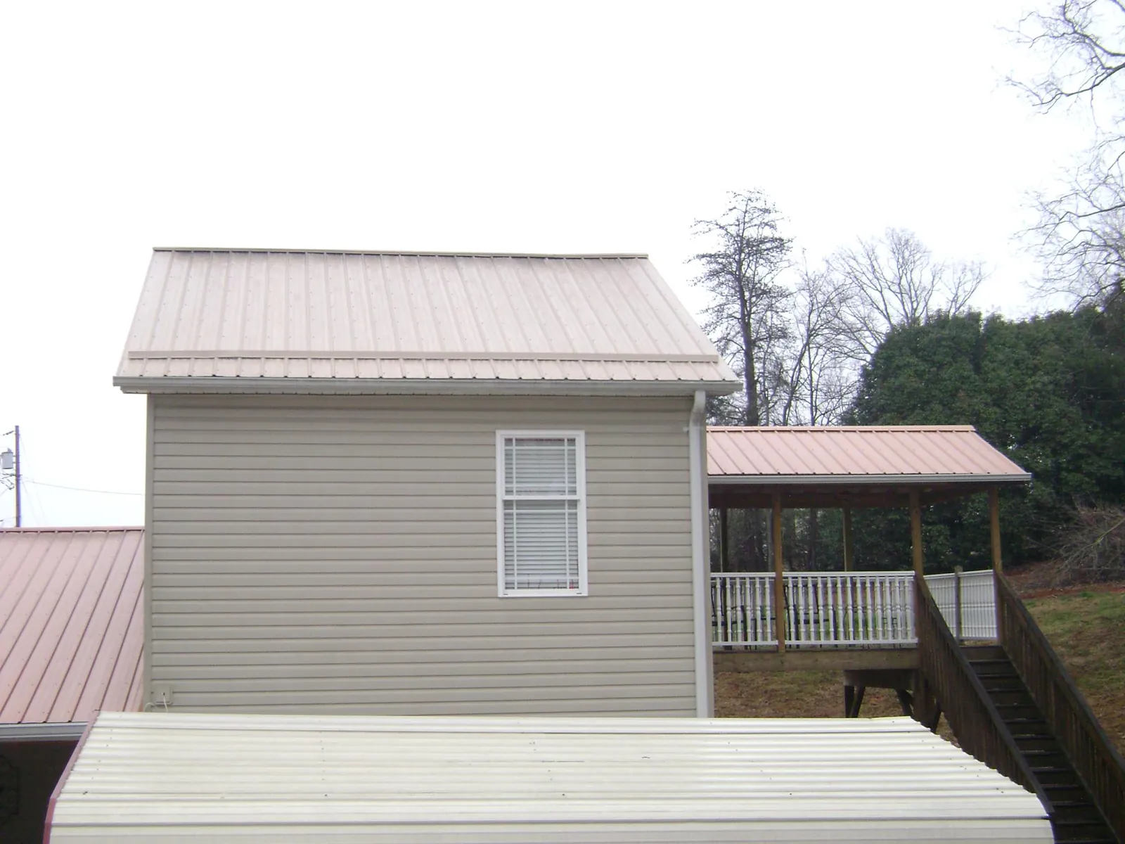 Tan metal roofs on a two story addition and attached porch, from a Roof Replacement job in Piedmont